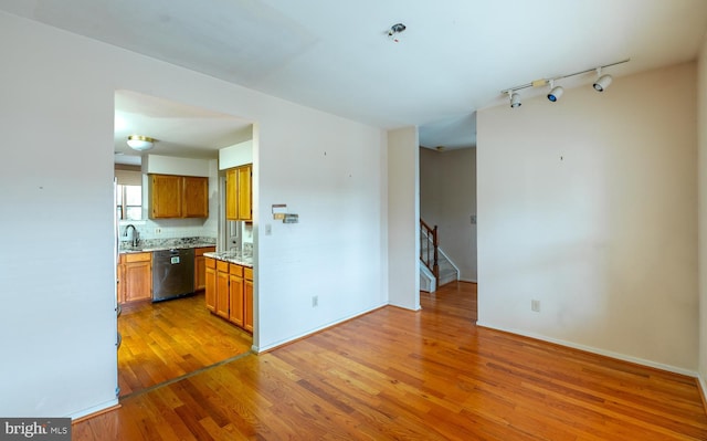 kitchen featuring sink, rail lighting, stainless steel dishwasher, backsplash, and hardwood / wood-style floors