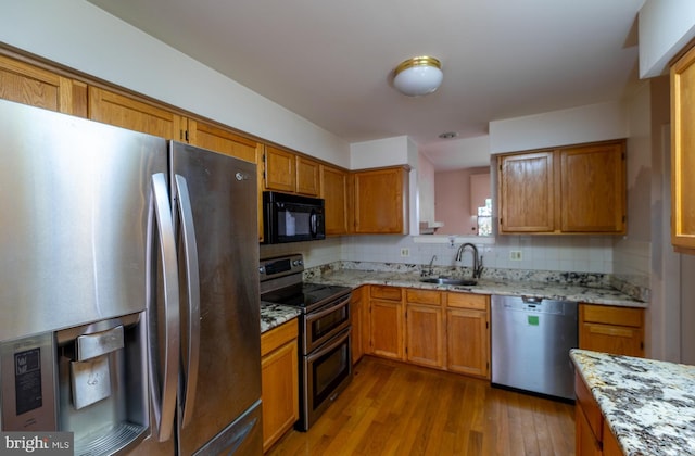 kitchen with sink, light stone counters, backsplash, light hardwood / wood-style floors, and appliances with stainless steel finishes