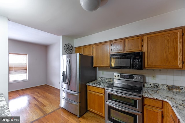 kitchen featuring light stone countertops, light wood-type flooring, appliances with stainless steel finishes, and tasteful backsplash