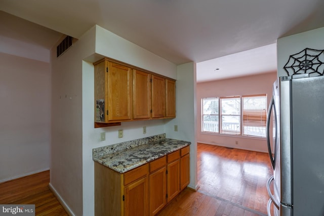 kitchen featuring light hardwood / wood-style flooring, stainless steel refrigerator, and light stone counters