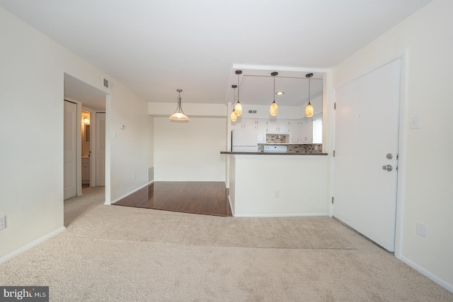 kitchen featuring light carpet, decorative backsplash, decorative light fixtures, white fridge, and white cabinetry