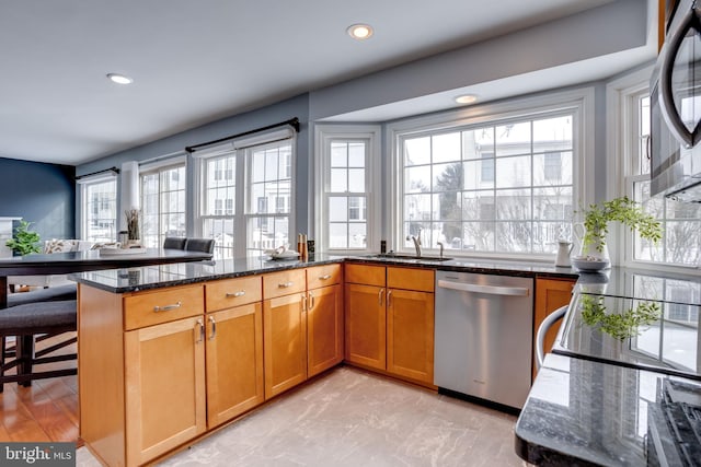 kitchen with kitchen peninsula, sink, stainless steel appliances, and dark stone countertops