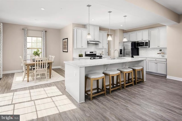 kitchen with light wood-type flooring, a breakfast bar, stainless steel appliances, a kitchen island with sink, and hanging light fixtures