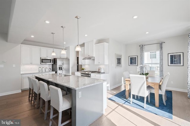 kitchen featuring a center island with sink, white cabinets, hanging light fixtures, light hardwood / wood-style flooring, and appliances with stainless steel finishes