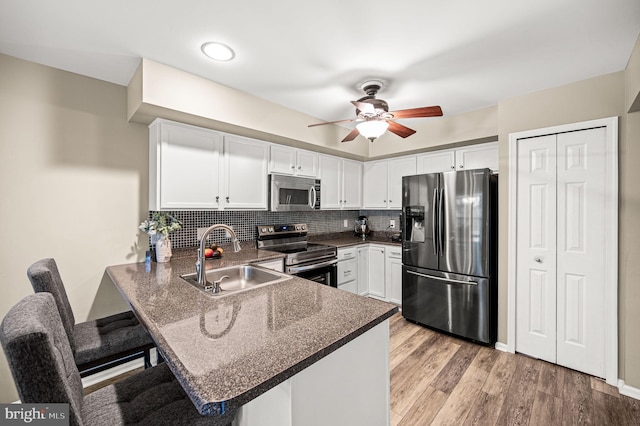 kitchen with a breakfast bar, sink, light wood-type flooring, kitchen peninsula, and stainless steel appliances