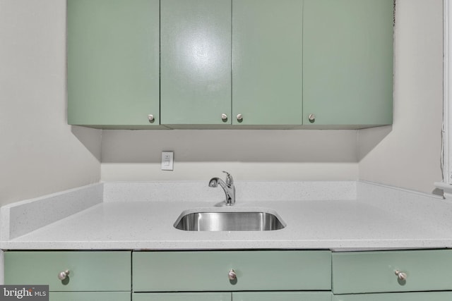 kitchen with light stone countertops, sink, and green cabinetry