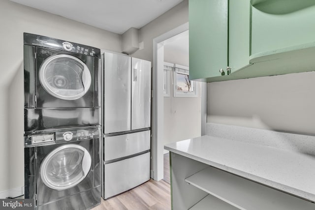 washroom featuring stacked washer / drying machine, light hardwood / wood-style flooring, and cabinets