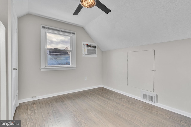 additional living space with vaulted ceiling, a textured ceiling, a wall unit AC, ceiling fan, and hardwood / wood-style floors