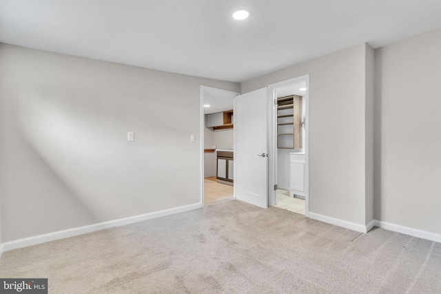 unfurnished bedroom with light colored carpet, ensuite bathroom, a spacious closet, and a closet