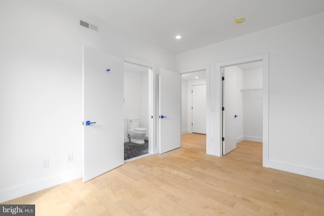 unfurnished bedroom featuring ensuite bath, a spacious closet, a closet, and light wood-type flooring