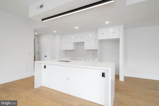 kitchen with a kitchen island, tasteful backsplash, white cabinetry, and light hardwood / wood-style flooring