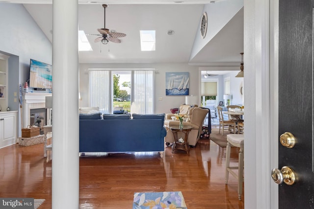 living room with ceiling fan, wood-type flooring, vaulted ceiling with skylight, and a fireplace