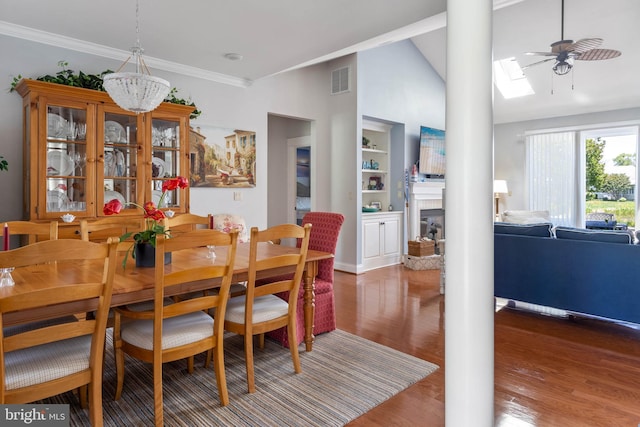 dining area with crown molding, dark hardwood / wood-style flooring, ceiling fan, vaulted ceiling with skylight, and a tiled fireplace