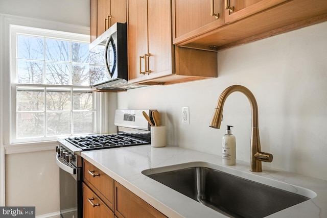 kitchen with light stone counters, brown cabinets, stainless steel appliances, and a sink