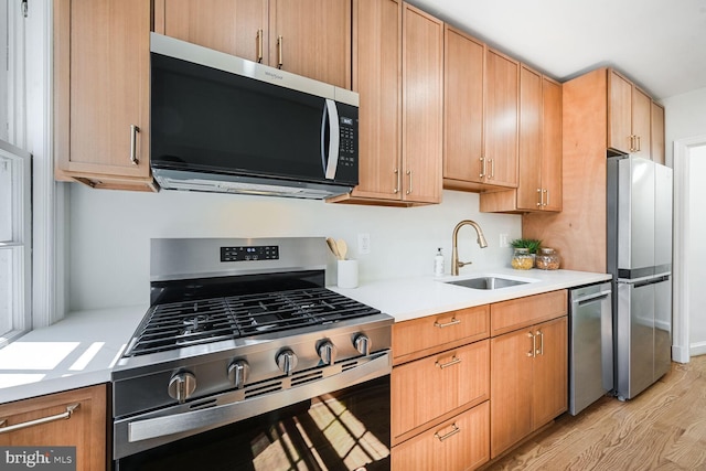 kitchen with a sink, stainless steel appliances, light wood-type flooring, and light countertops