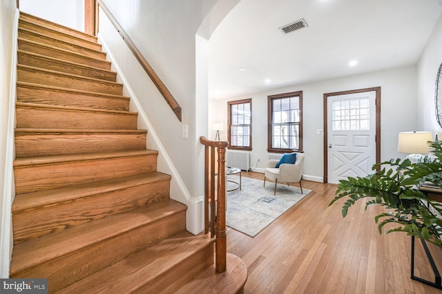 foyer with light wood-type flooring, visible vents, arched walkways, radiator, and stairs