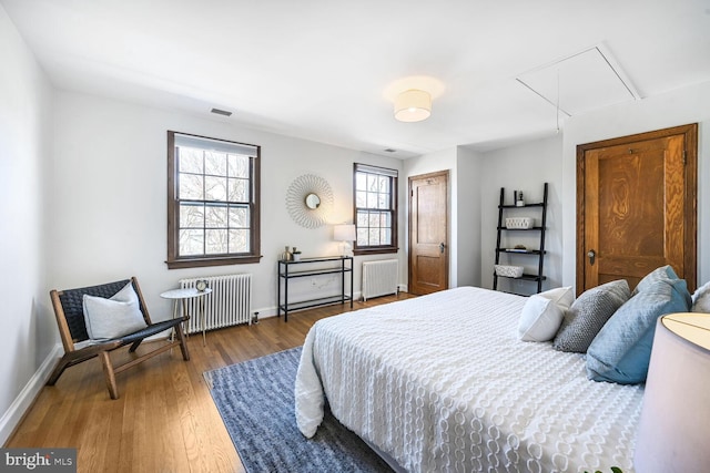 bedroom with radiator, attic access, baseboards, and wood finished floors