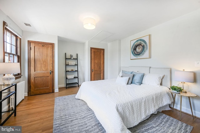 bedroom with attic access, light wood-style flooring, visible vents, and baseboards