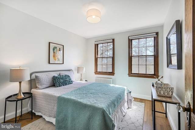 bedroom featuring baseboards, multiple windows, radiator, and wood finished floors