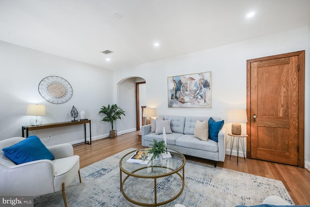 living area featuring recessed lighting, visible vents, arched walkways, and wood finished floors