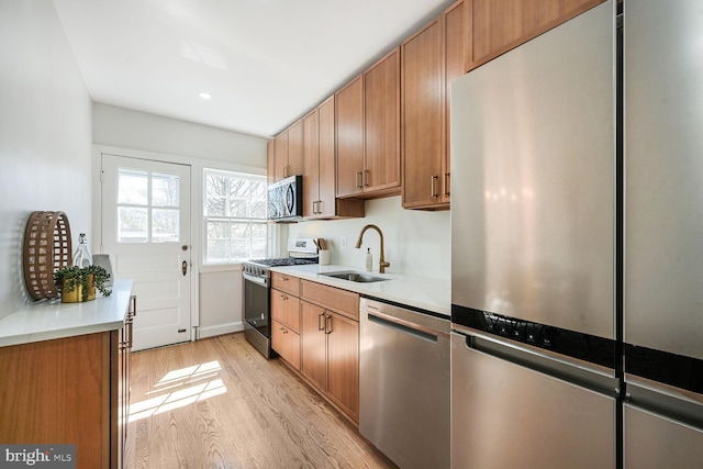 kitchen featuring light wood-style flooring, a sink, stainless steel appliances, light countertops, and brown cabinets