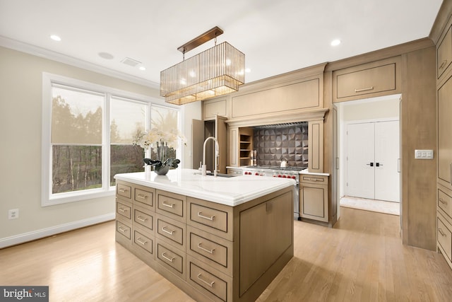 kitchen with high end range, a center island with sink, crown molding, light wood-type flooring, and decorative light fixtures