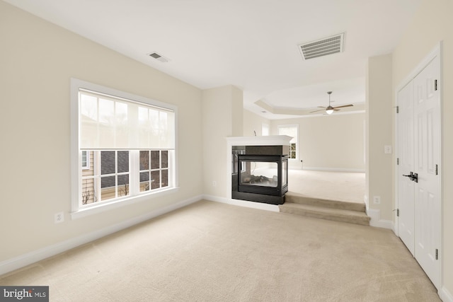 unfurnished living room with a multi sided fireplace, light carpet, plenty of natural light, and ceiling fan