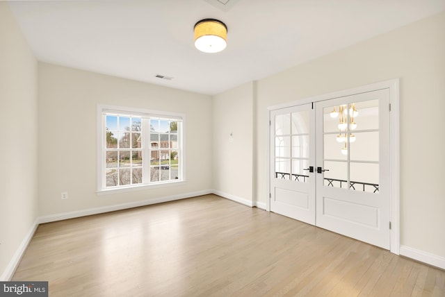 empty room with a chandelier, french doors, and light hardwood / wood-style flooring