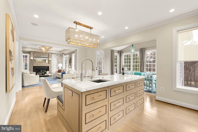 kitchen featuring a kitchen island with sink, light brown cabinetry, hanging light fixtures, and light hardwood / wood-style floors