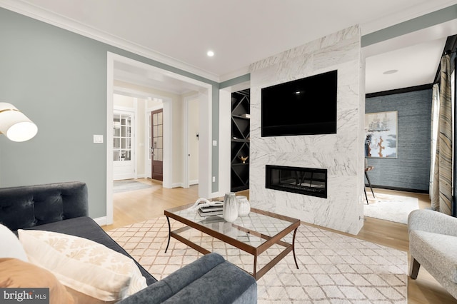 living room with a fireplace, built in shelves, light wood-type flooring, and crown molding