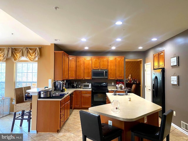 kitchen with kitchen peninsula, a breakfast bar, sink, black appliances, and light tile patterned floors