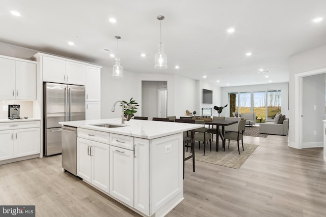 kitchen featuring sink, hanging light fixtures, stainless steel appliances, a kitchen island with sink, and white cabinets