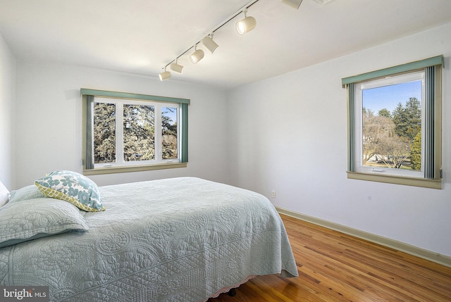 bedroom with multiple windows, rail lighting, and hardwood / wood-style flooring