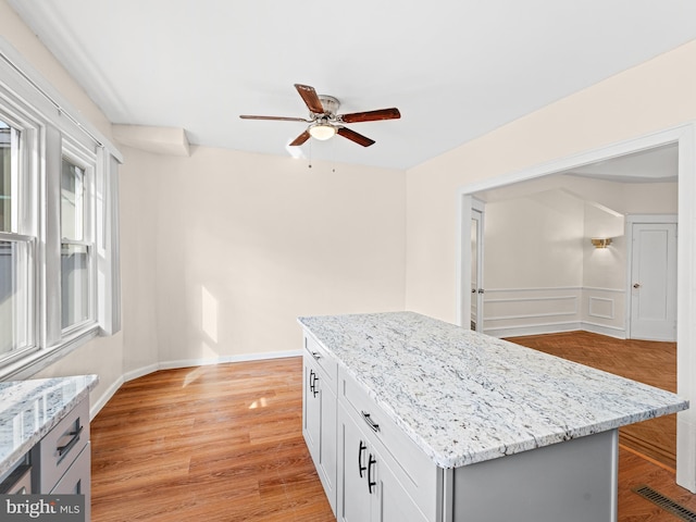 kitchen with ceiling fan, a center island, light stone countertops, and light hardwood / wood-style flooring