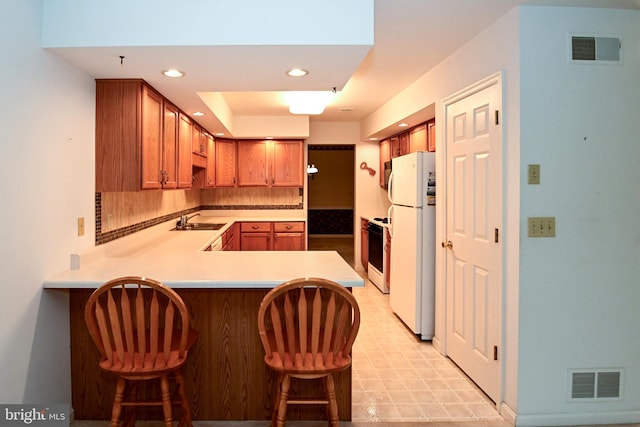 kitchen with sink, tasteful backsplash, kitchen peninsula, white appliances, and a breakfast bar area