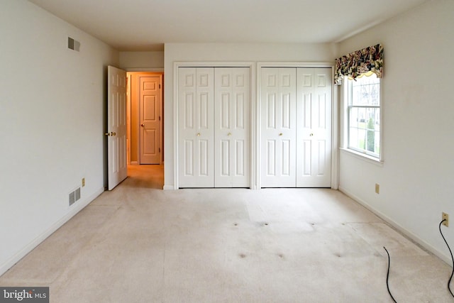 unfurnished bedroom with light colored carpet and two closets