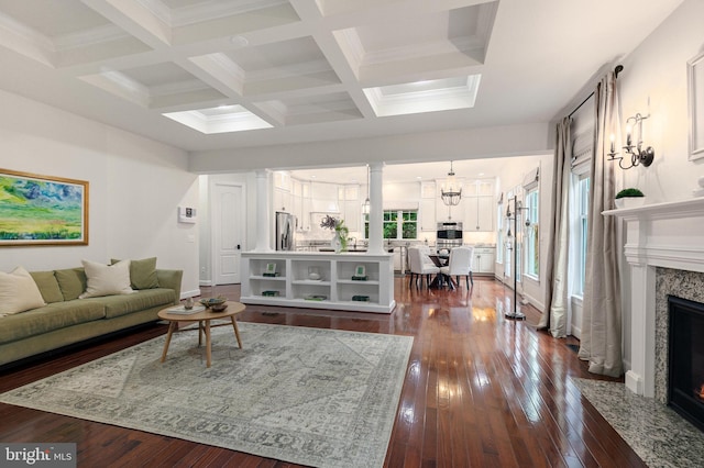 living room with dark wood-type flooring, coffered ceiling, a premium fireplace, beamed ceiling, and a notable chandelier