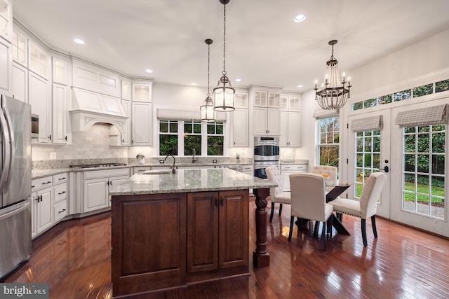 kitchen featuring appliances with stainless steel finishes, french doors, a kitchen island with sink, dark hardwood / wood-style floors, and hanging light fixtures