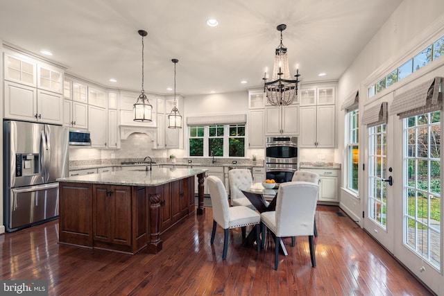 kitchen with light stone countertops, a kitchen island with sink, dark wood-type flooring, and stainless steel appliances