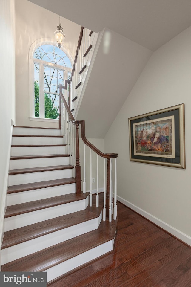 stairway featuring wood-type flooring, vaulted ceiling, and an inviting chandelier