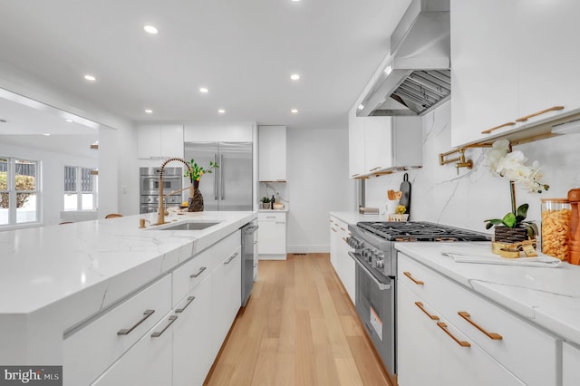 kitchen with exhaust hood, white cabinetry, light hardwood / wood-style floors, premium appliances, and light stone countertops