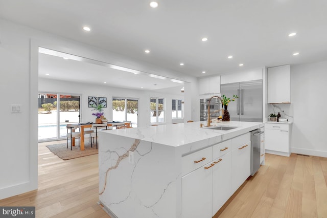 kitchen featuring an island with sink, light stone counters, white cabinetry, and stainless steel appliances