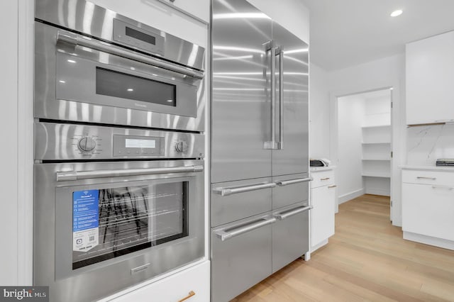 kitchen with decorative backsplash, white cabinets, stainless steel appliances, and light wood-type flooring