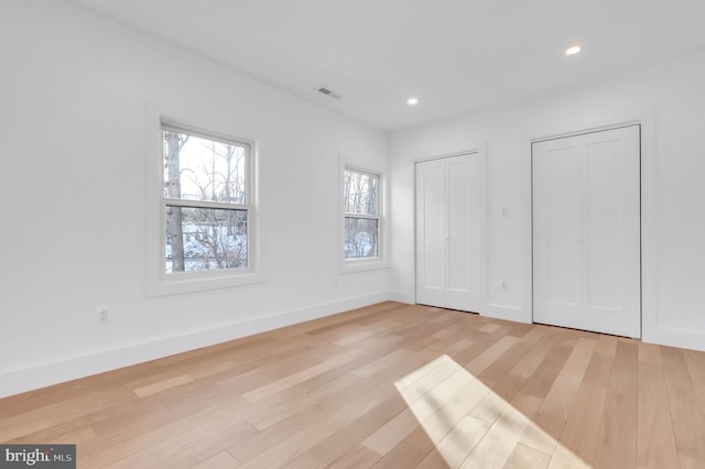 unfurnished bedroom with two closets and light hardwood / wood-style floors