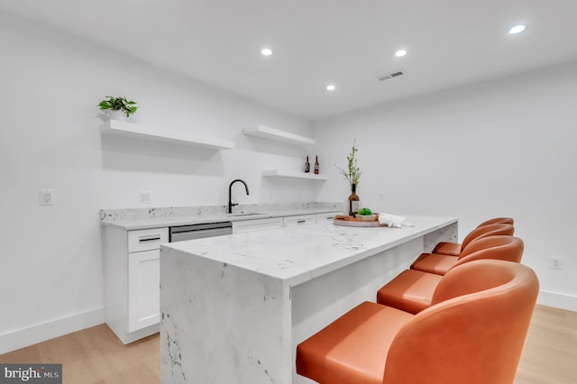 kitchen featuring light stone countertops, a kitchen island, white cabinetry, light hardwood / wood-style floors, and a breakfast bar