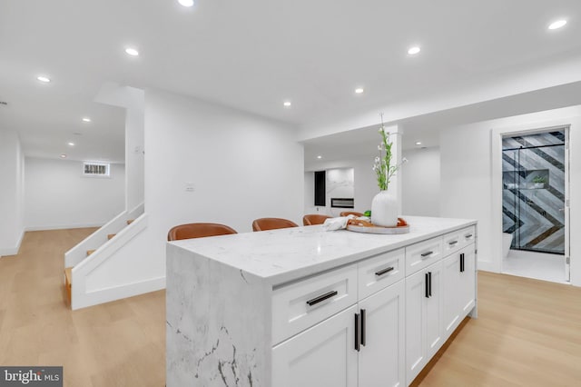 kitchen with a center island, a kitchen bar, white cabinetry, light hardwood / wood-style floors, and light stone counters