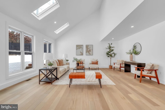 living room with high vaulted ceiling, a skylight, plenty of natural light, and light hardwood / wood-style flooring