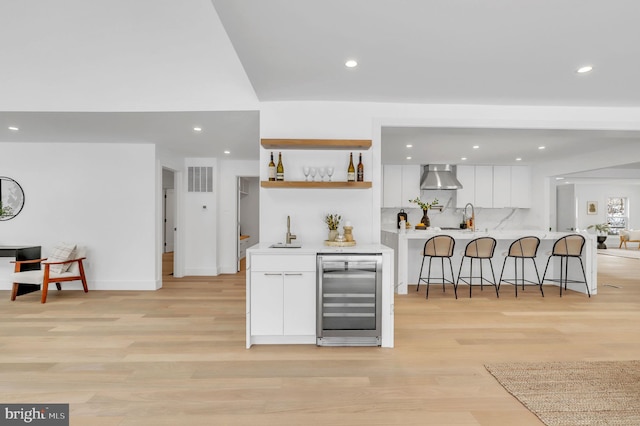 kitchen with white cabinetry, wine cooler, a breakfast bar, and wall chimney range hood