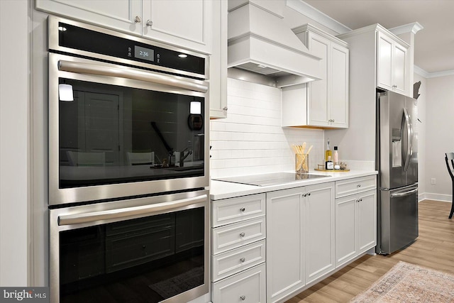 kitchen with appliances with stainless steel finishes, light wood-type flooring, white cabinets, custom exhaust hood, and ornamental molding