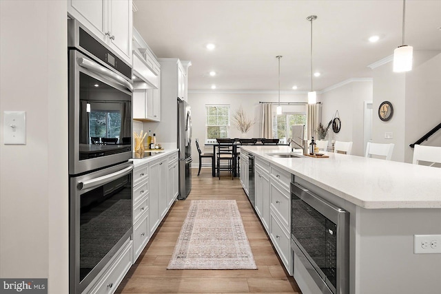 kitchen featuring pendant lighting, white cabinets, ornamental molding, a large island, and stainless steel appliances